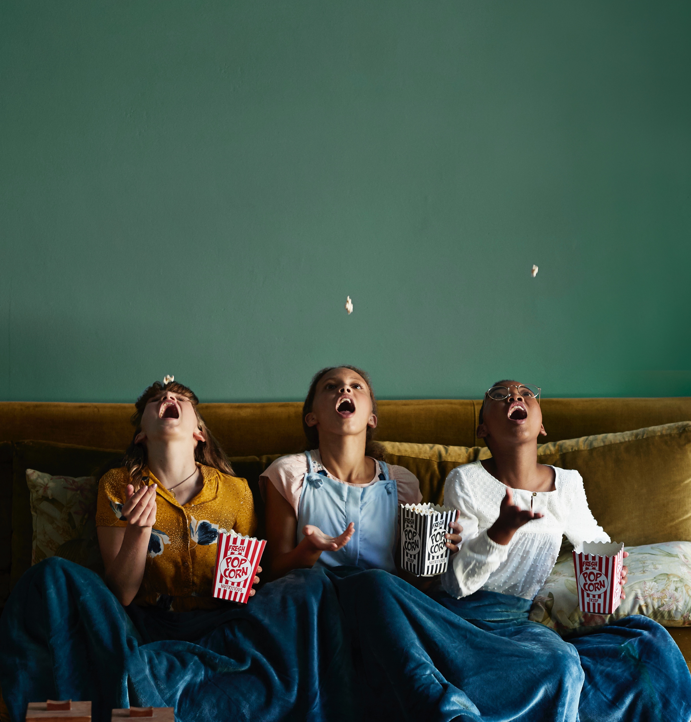 Three kids on a couch trying to catch popcorn in their mouths