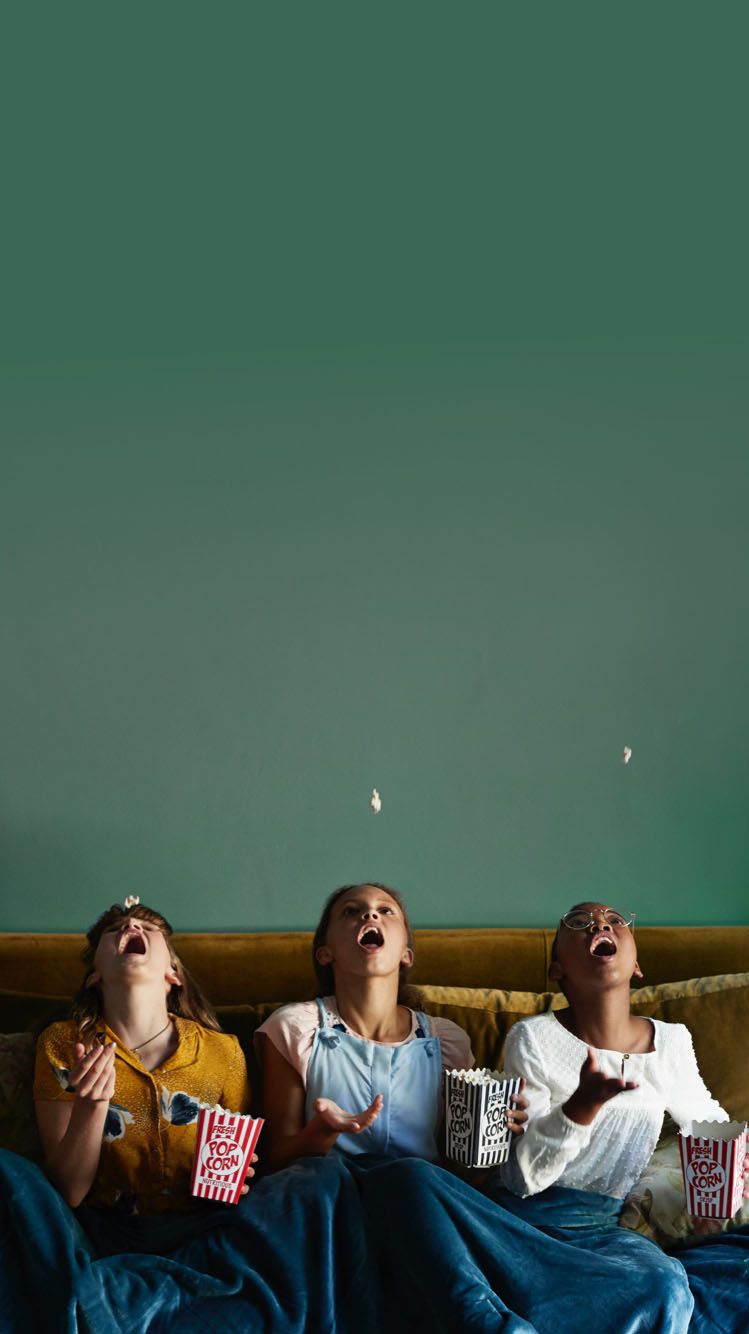 Three kids on a couch trying to catch popcorn in their mouths